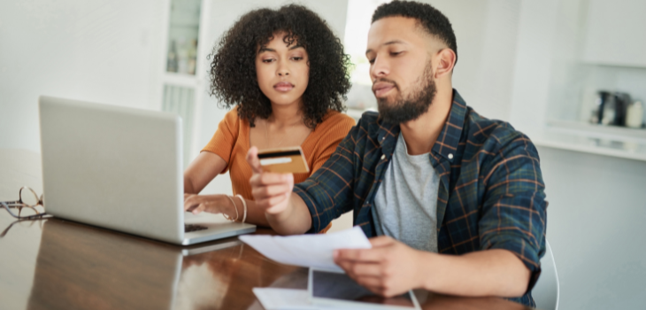 A young couple sits at their desk with their credit cards and computer, creating a plan to pay off their credit card debts quickly.